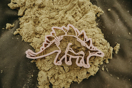 Pink dinosaur-shaped cookie cutter on green play dough