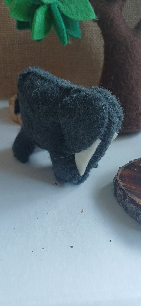 Small felt elephant toy on a white surface with a blurred background