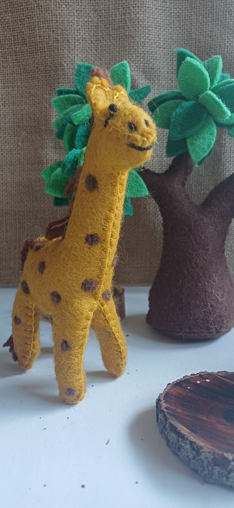 Felt Yellow giraffe toy with green leaves and a brown tree on a white surface.