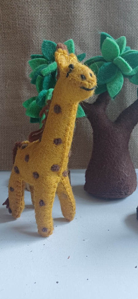 Toy giraffe with green leaves and a brown tree on a white surface