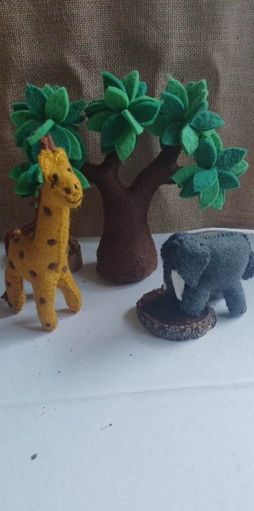 Felt toy animals including a giraffe, tree, and elephant on a white surface with a brown background.