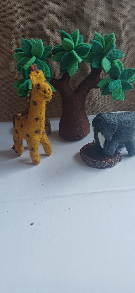Felt animal toys including a giraffe, elephant, and tree on a white surface with a brown background.