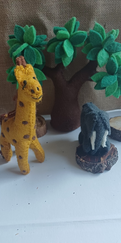 Two small felt animal figurines on a white surface with green felt trees in the background.