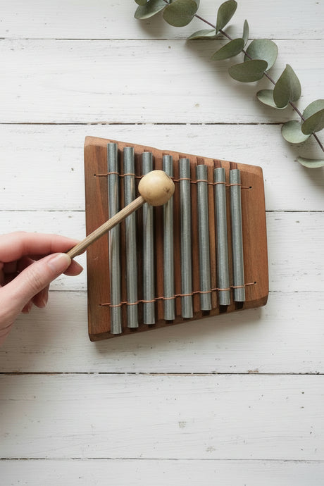 Hand holding a wooden xylophone with metal bars on a textured surface