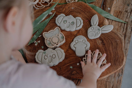 Child interacting with animal-shaped playdough cutters on a wooden board