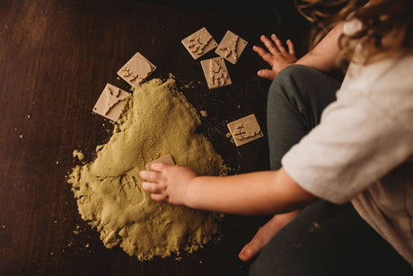 Child playing with green kinetic sand on a dark surface