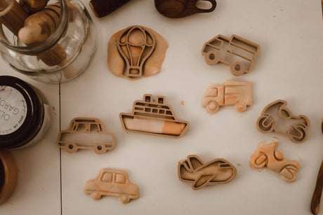 Collection of wooden cookie cutters shaped like vehicles on a white surface.