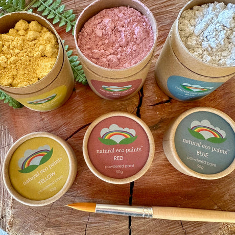 Bowls of natural eco paint powders on a wooden surface with a brush.