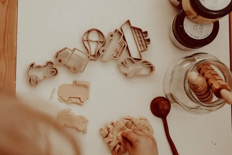 Cookie cutters and dough on a table with a jar of flour and wooden spoon.