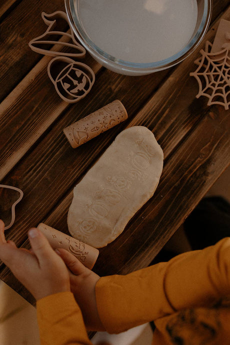 Wooden Halloween cookie cutters on a wooden table with a child's hands interacting with them.