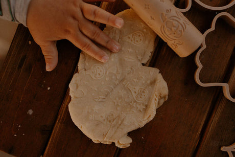 Childs hand pressing a cookie cutter into dough on a wooden surface