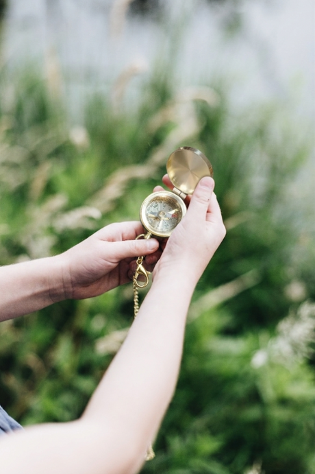Hand holding a compass with a blurred natural background