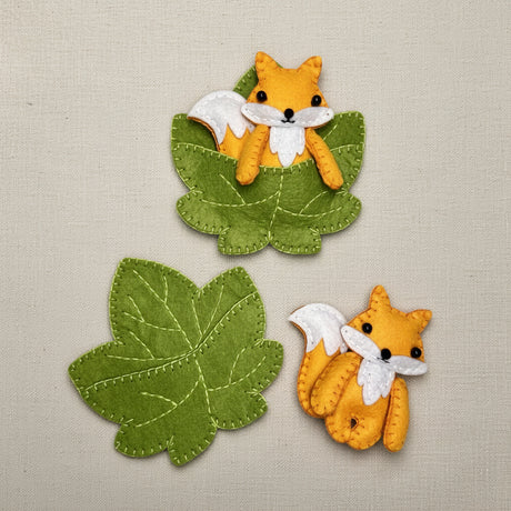 Two felt foxes and two green leaves on a white background