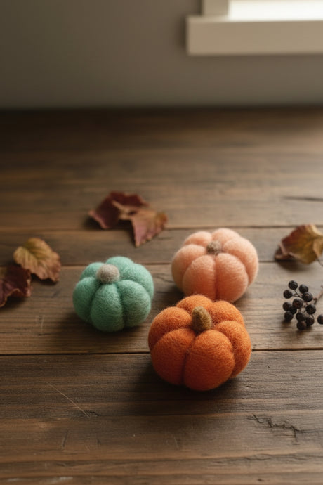 Three small felted wool pumpkins in mint green, orange, and peach, arranged on a dark gray fabric background.