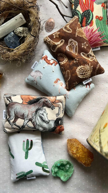 A styled flat-lay of five small sandbags for kidswestern and desert-themed prints, arranged on a textured light fabric alongside crystals and a woven basket.