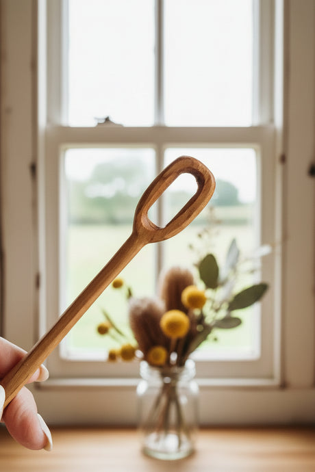 Wooden bubble blower in a glass jar with a hand holding one spoon against a neutral background
