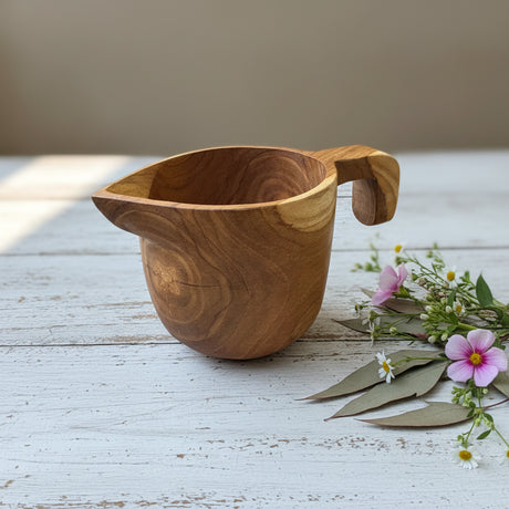 Wooden cup with handle on a wooden surface with flowers in the background