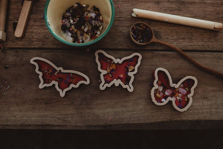 Butterfly-shaped playdough cutters on a wooden surface with a bowl and spoon in the background.
