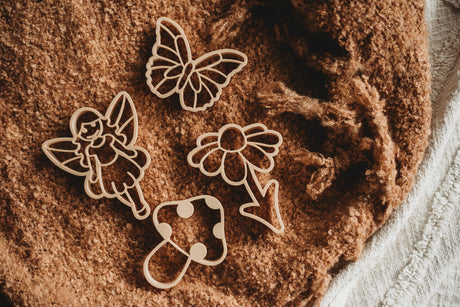 Wooden butterfly, fairy, and heart-shaped cookie cutters on a brown surface.