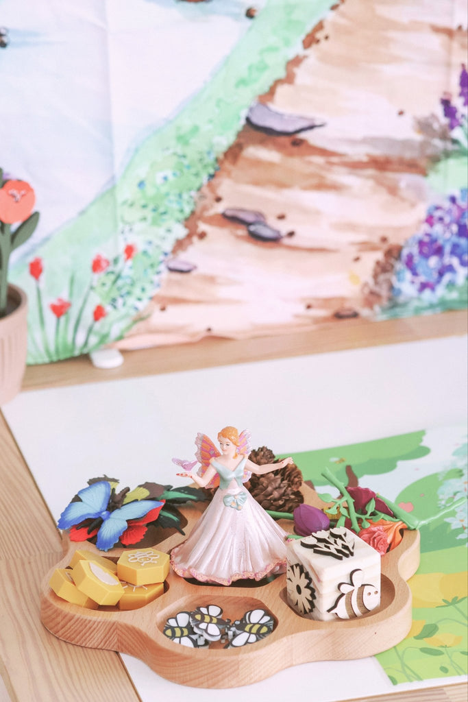 Wooden tray with fairy figurine, flowers, sensory stamps on a scenic background