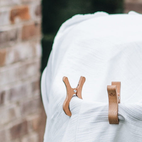 Two wooden play clips attached to a white fabric, with a blurred background featuring a brick wall.