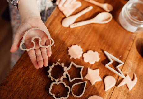 Person holding a cloud-shaped cookie cutter with cut-out shapes on a wooden table.