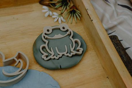 Frog-shaped clay mold on a wooden surface with floral decorations.