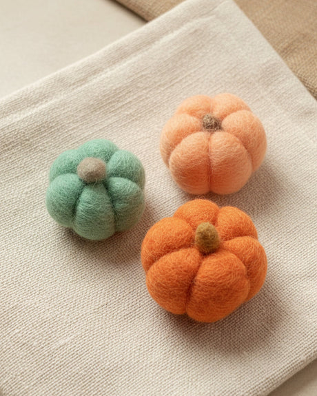 Three small felted wool pumpkins in mint green, orange, and peach, arranged on white background