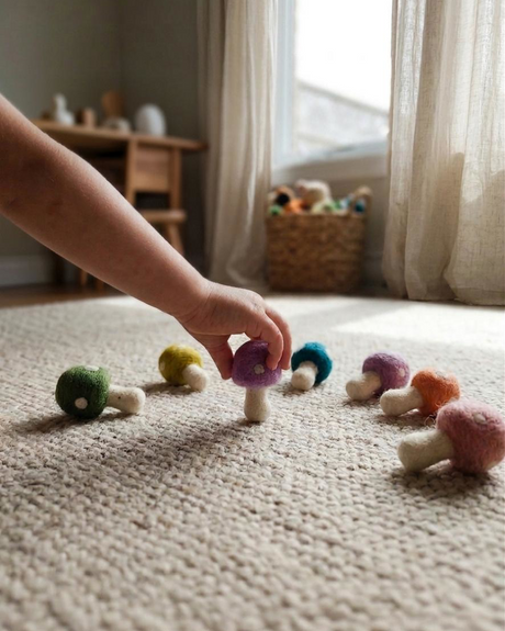 Child's hand reaching for colorful felt mushrooms on a carpeted floor.