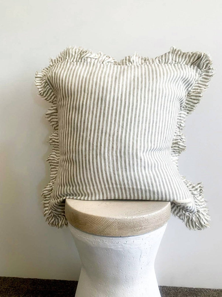 Striped pillow with ruffled edges on a white pedestal against a plain background