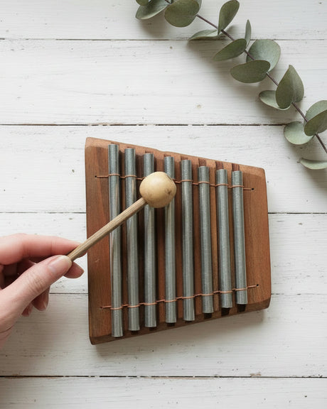 Hand holding a wooden xylophone with metal bars on a textured surface
