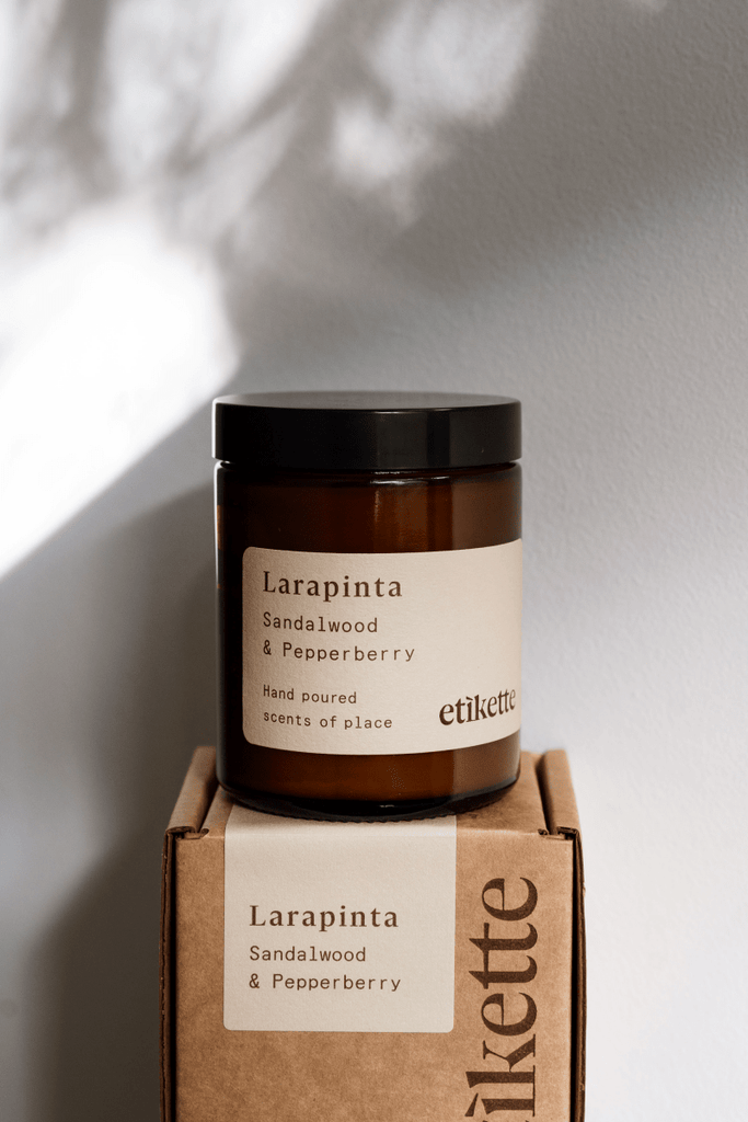 Candle jar labeled 'Larapinta Sandalwood & Pepperberry' by 'etikette' on a cardboard box with the same label.