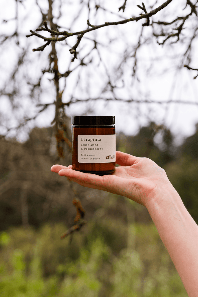 Hand holding a jar labeled 'Larapinta' against a blurred natural background