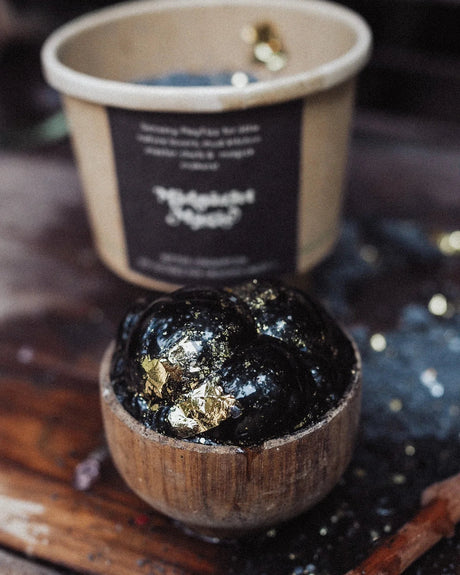 A kraft paper cup labeled 'Midnight Moss' filled with dark moss, shown on a rustic wooden surface with a small wooden bowl, a wooden spoon, and scattered moss pieces.