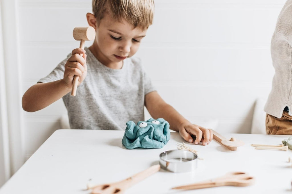 Child playing with play dough and tools on a white table