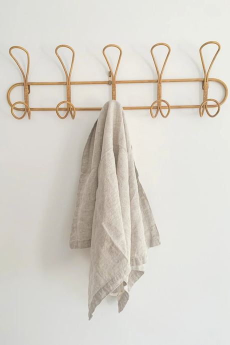 Rattan coat rack with a natural tea-towel hanging on it against a white background