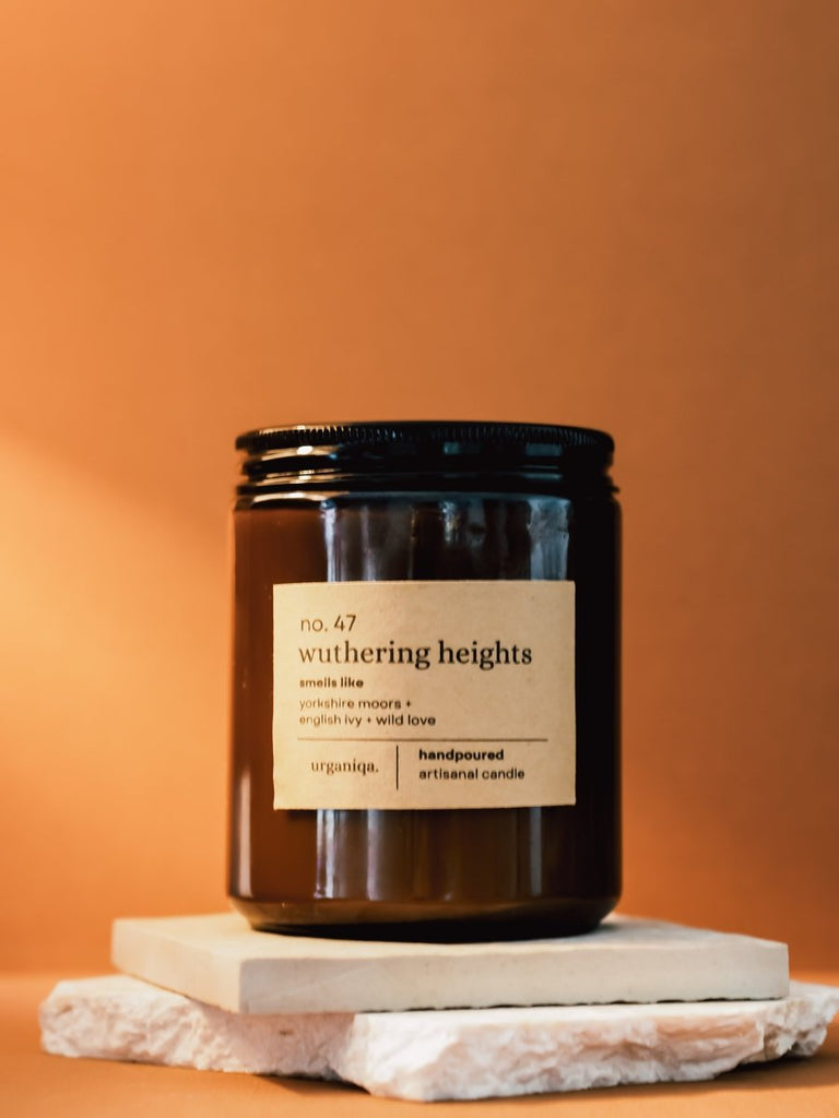 Candle jar labeled 'no. 47 wuthering heights' on a marble stand with an orange background