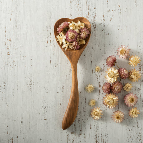 Wooden heart-shaped spoon and dish with dried flowers on a white background