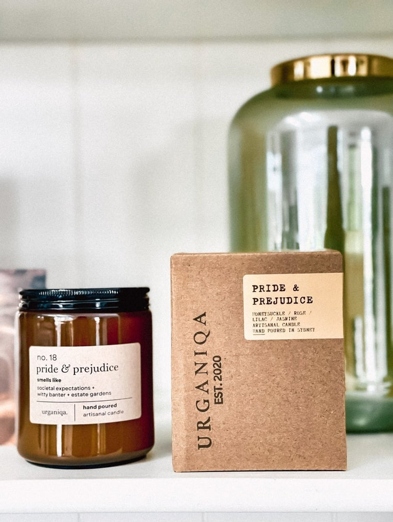 Candle jar and box labeled 'Pride & Prejudice' by Urganiqa on a white surface.