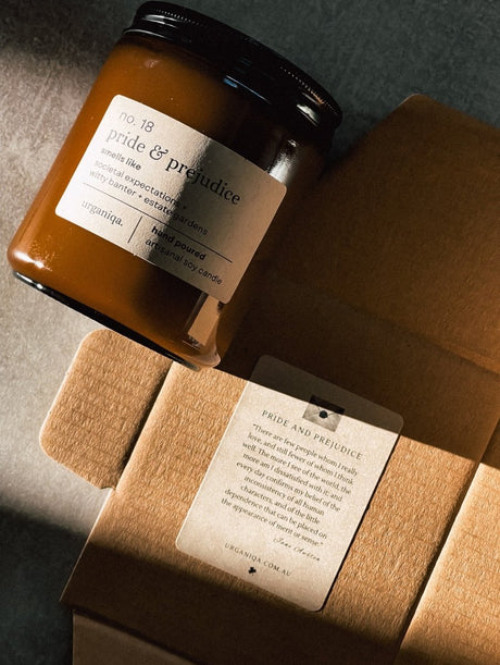 Candle jar labeled ' pride & prejudice' with a matching box on a textured surface