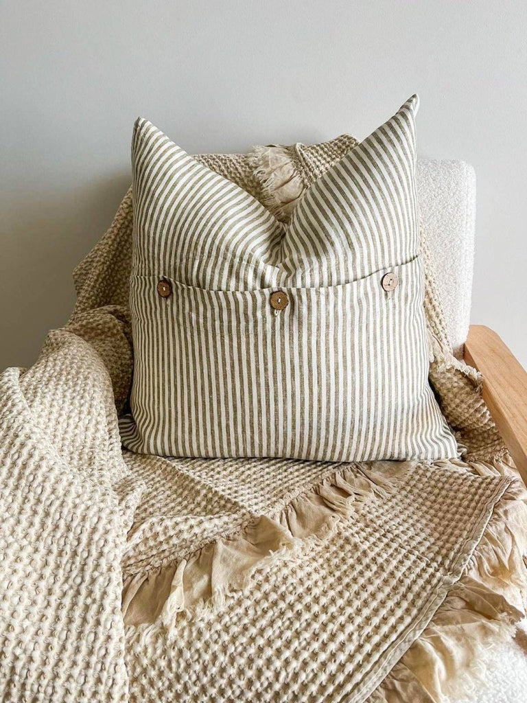Striped cushion with buttons on a textured blanket against a neutral background