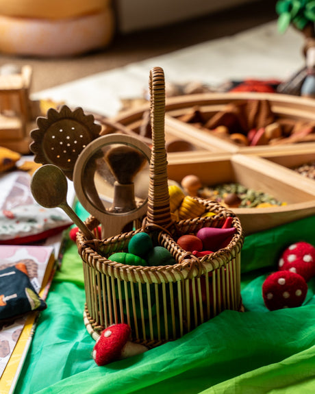 Wicker basket with wooden toys and colorful items on a green surface