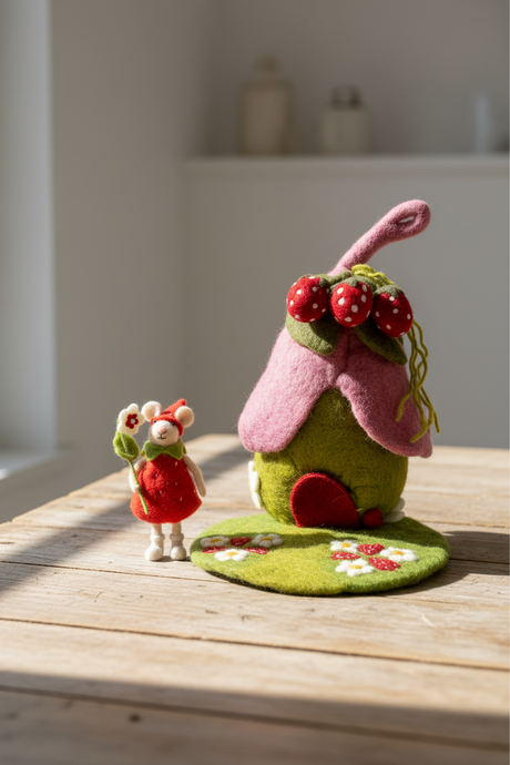 Felt fairy house with pink roof and green body, accompanied by a fairy figure holding a candy cane on a white background.