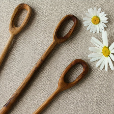 Three wooden spoon-like utensils with oval handles arranged diagonally on a gray textured surface next to a white daisy flower.