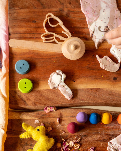 Children's toys and items on a wooden surface with a child's hand interacting.