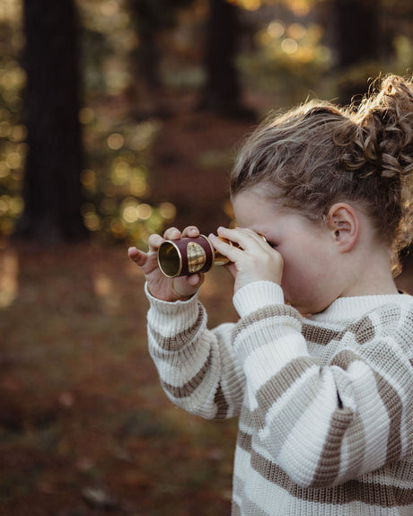 Child holding a vintage brass ttelescope in a forest setting