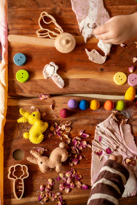 Children's toys and items on a wooden surface with a child's hand interacting.