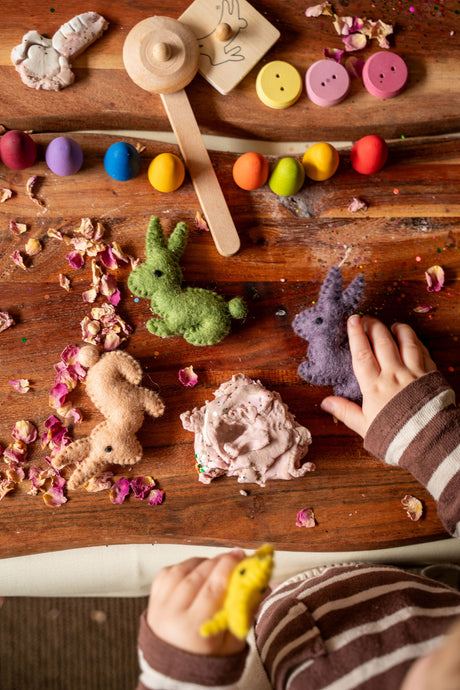 Children's play area with colorful buttons, felt toys, and a child's hand interacting with the items on a wooden surface.